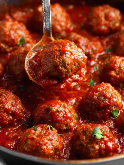 A spoon is in a bowl of meatballs.