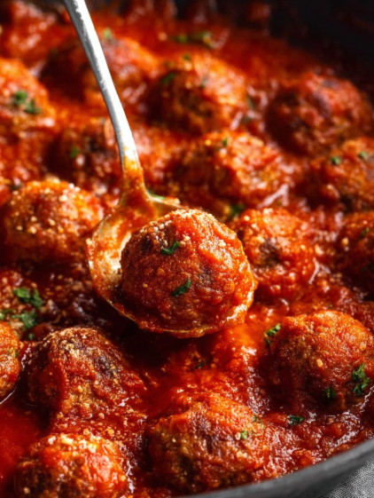 A spoon is in a bowl of meatballs.