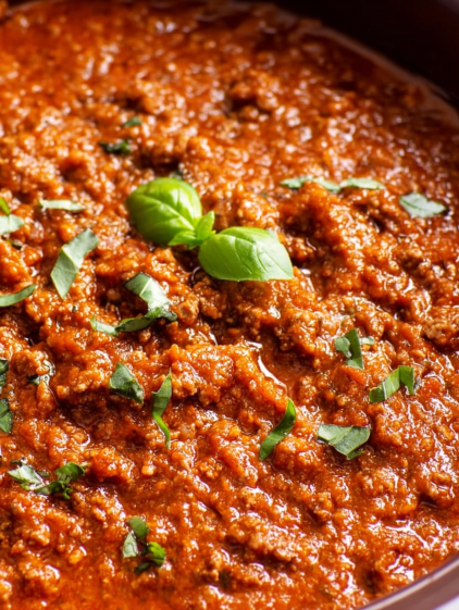 A close up of a bowl of red sauce with green leaves on top.