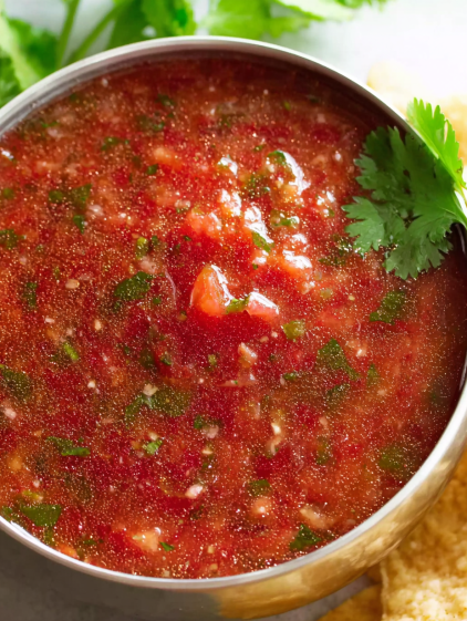 A bowl of salsa with tomatoes and green herbs.