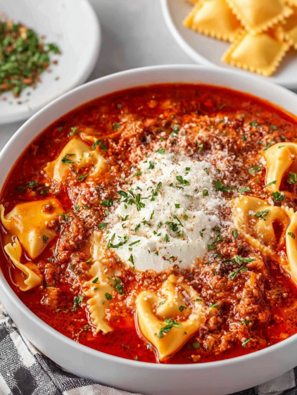 A bowl of red soup with pasta and white cheese on top.