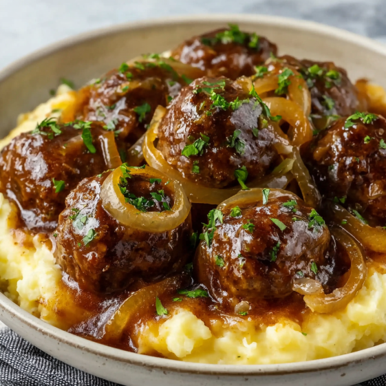 A bowl of meatballs with onions and herbs.