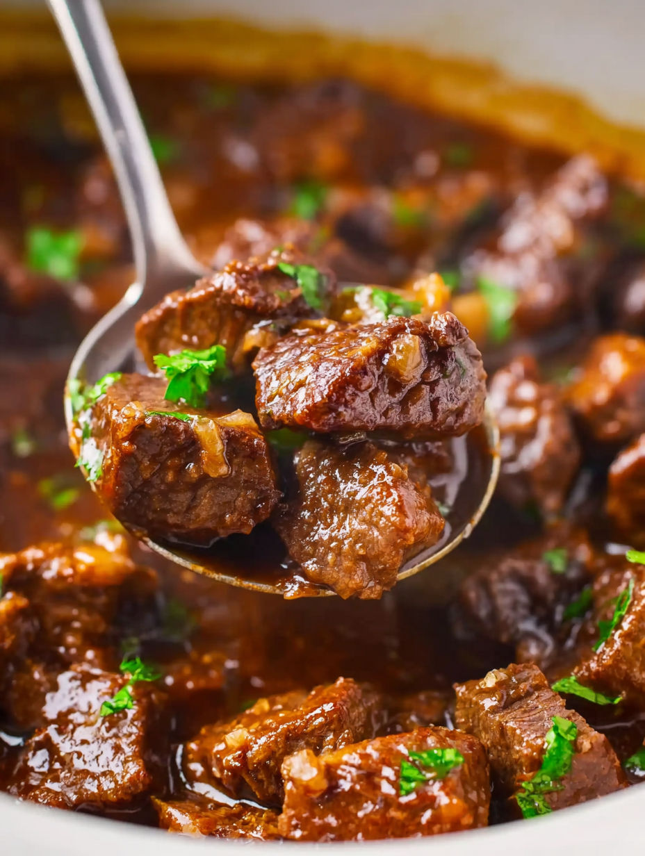 A spoon is in a bowl of steak bites.