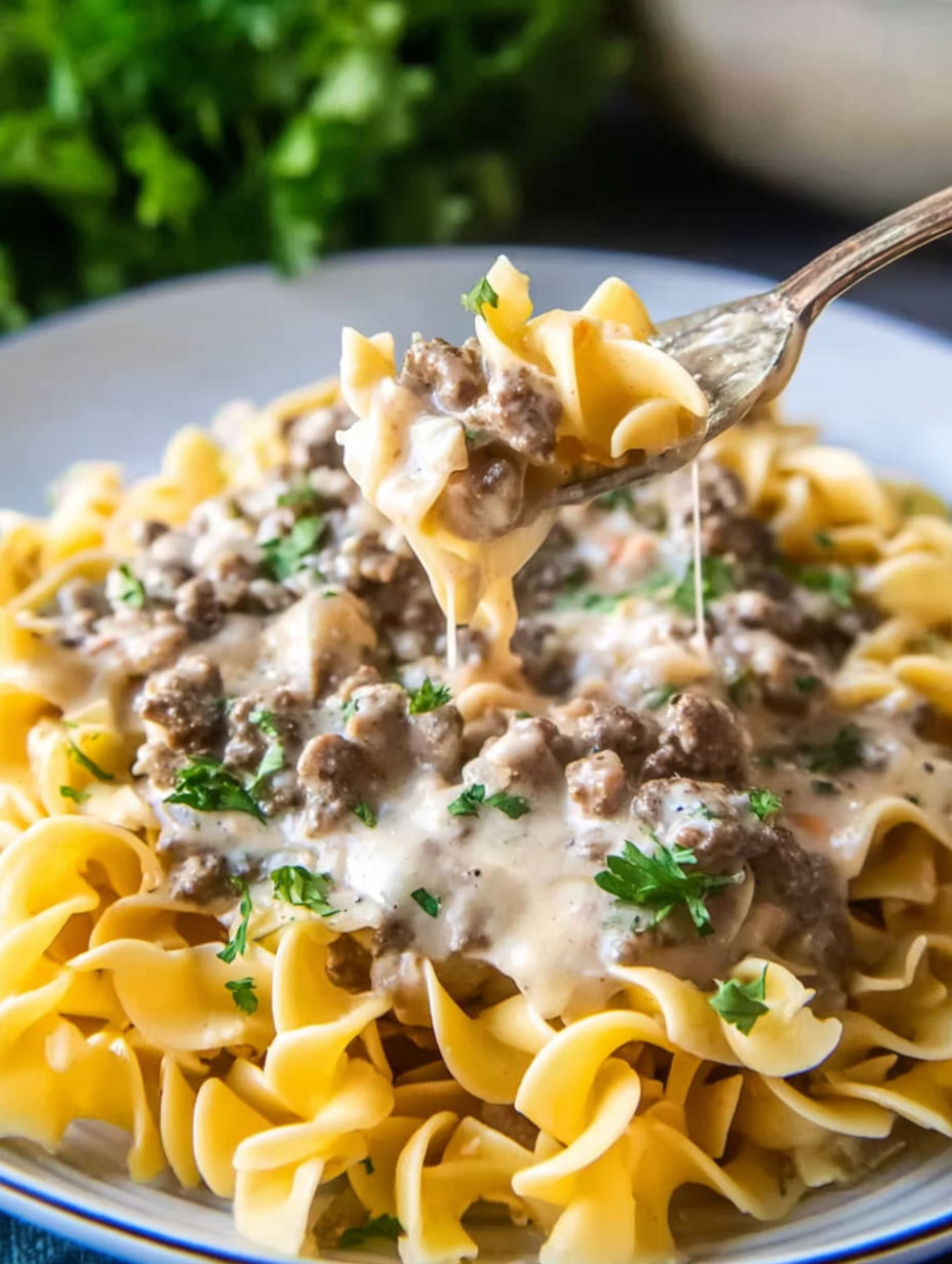 A fork is being used to eat a bowl of ground beef stroganoff.