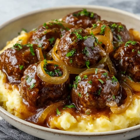 A bowl of meatballs with onions and herbs.