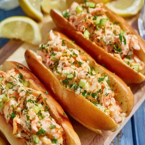 Two shrimp rolls with lemon wedges on a table.