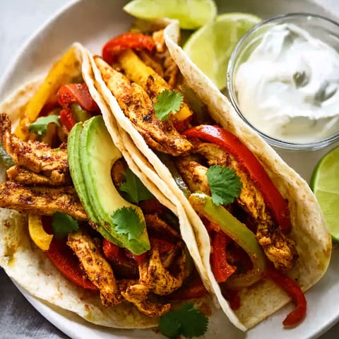 A plate of chicken fajitas with a side of sour cream.