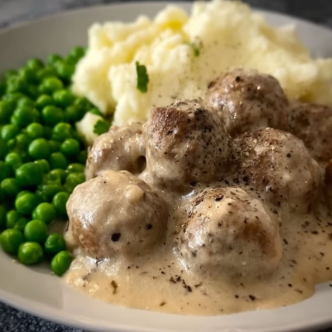 A plate of Swedish meatballs with peas and potatoes.
