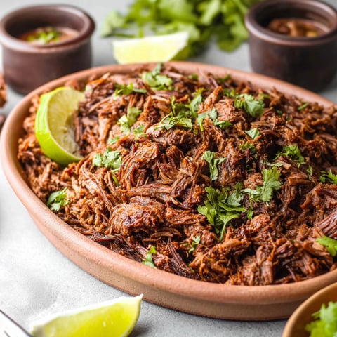 A bowl of beef with lime wedges on the side.
